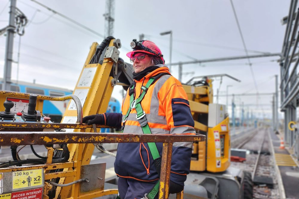 Opératrice en nacelle rail-route, harnais et équipements de protection, sur un faisceau de voies électrifiées